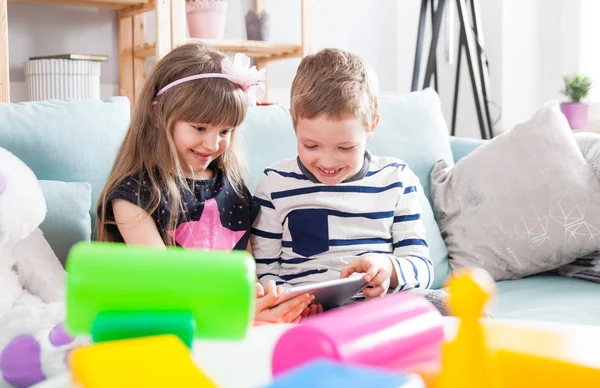 Irmãos sentados no sofá em casa e brincando com tablet pc juntos — Fotografia de Stock