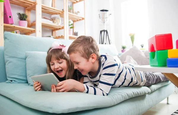 Evde koltukta yalan ve tablet ile birlikte oynayan mutlu kardeşler