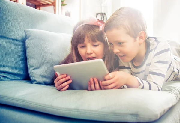 Evde koltukta yalan ve tablet ile birlikte oynayan mutlu kardeşler