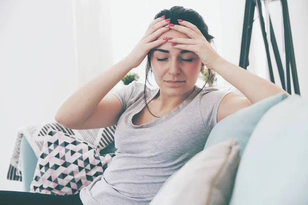 Young worried woman with headache while sitting on comfortable sofa — Stock Photo, Image