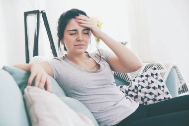 Genç kadın baş ağrısı ile rahat koltukta otururken endişeli