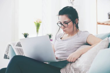 Ev rahat koltukta otururken dizüstü bilgisayar kullanan genç kadın