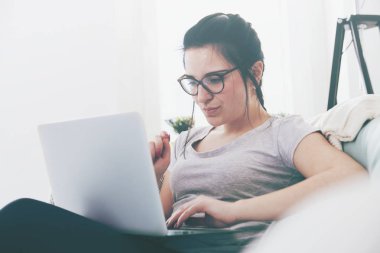 Ev rahat koltukta otururken dizüstü bilgisayar kullanan genç kadın