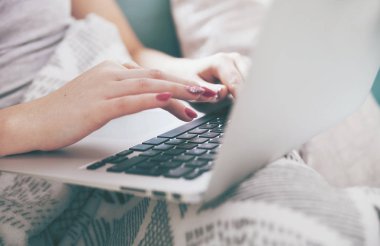 Evde kanepede otururken dizüstü bilgisayar kullanan kadın