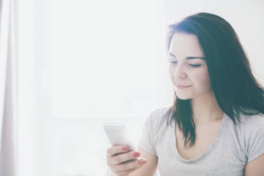 Evde rahat koltukta otururken cep telefonu kullanan genç kadın