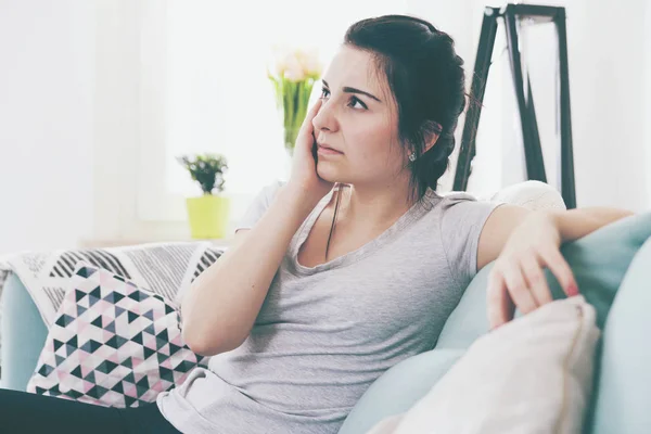 Young worried woman with headache while sitting on comfortable sofa — Stock Photo, Image