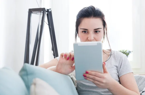 Junge Frau benutzt PC-Tablet während sie auf bequemem Sofa sitzt — Stockfoto