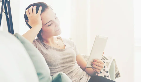 Wanita muda menggunakan tablet pc sambil duduk di sofa yang nyaman — Stok Foto