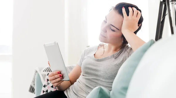 Mujer joven usando la tableta de la PC mientras que se sienta en sofá cómodo —  Fotos de Stock