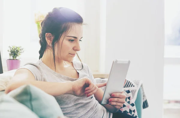 Mujer joven usando la tableta de la PC mientras que se sienta en sofá cómodo — Foto de Stock
