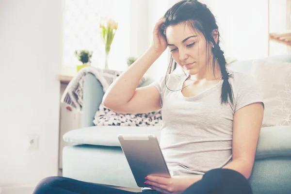 Jonge vrouw met behulp van tablet pc terwijl u zit in de buurt van comfortabele bank — Stockfoto