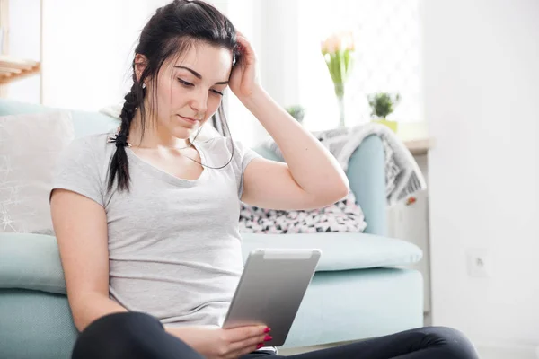 Mujer joven usando la tableta de la PC mientras que se sienta cerca cómodo sofá —  Fotos de Stock