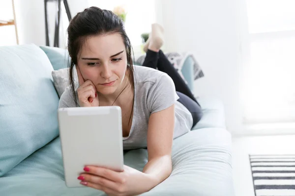 Junge Frau benutzt PC-Tablet während sie auf bequemem Sofa liegt — Stockfoto