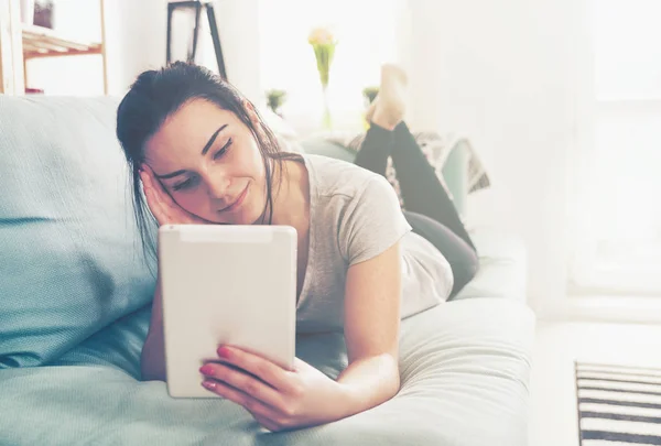 Mladá žena pomocí pc tablet vleže na pohodlném gauči — Stock fotografie