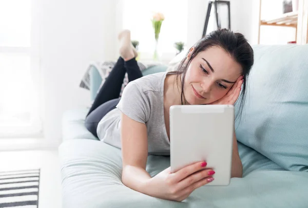 Junge Frau benutzt PC-Tablet während sie auf bequemem Sofa liegt — Stockfoto