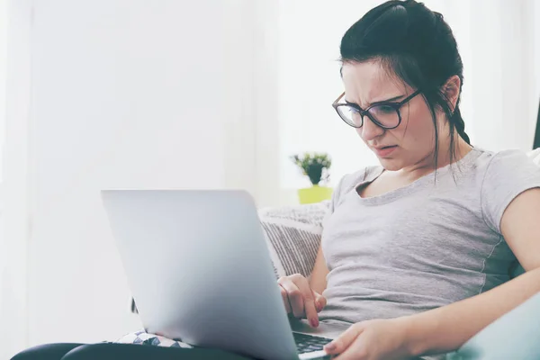Mladá žena pomocí přenosného počítače, zatímco sedí na pohodlné pohovce, domácí — Stock fotografie