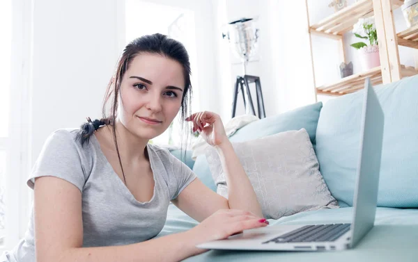 Jovem mulher usando laptop enquanto se senta perto de sofá confortável, casa — Fotografia de Stock