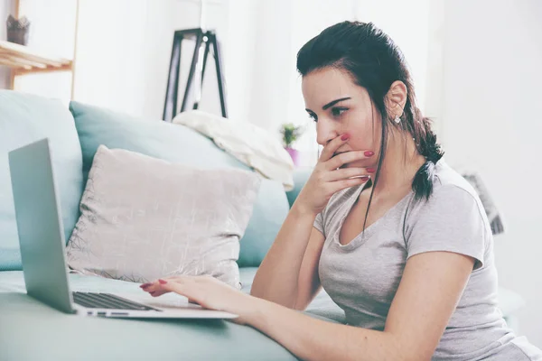 Junge Frau mit Laptop, während sie in der Nähe bequemes Sofa sitzt, zu Hause — Stockfoto