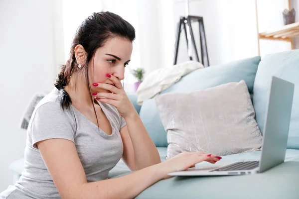 Junge Frau mit Laptop, während sie in der Nähe bequemes Sofa sitzt, zu Hause — Stockfoto