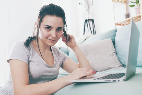 Junge Frau mit Laptop, während sie in der Nähe bequemes Sofa sitzt, zu Hause — Stockfoto