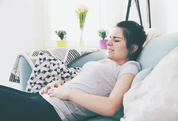 Junge Frau in Schmerzen, während sie auf bequemem Sofa sitzt, zu Hause — Stockfoto