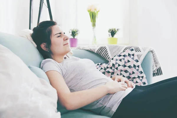 Wanita muda kesakitan sambil duduk di sofa yang nyaman, rumah — Stok Foto