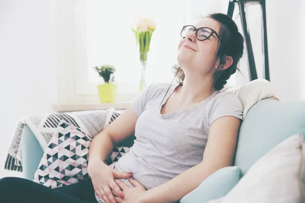 Young woman in pain while sitting on comfortable sofa, home — Stock Photo, Image