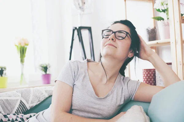 Jovem mulher relaxada sorrindo enquanto se senta no sofá confortável, em casa — Fotografia de Stock