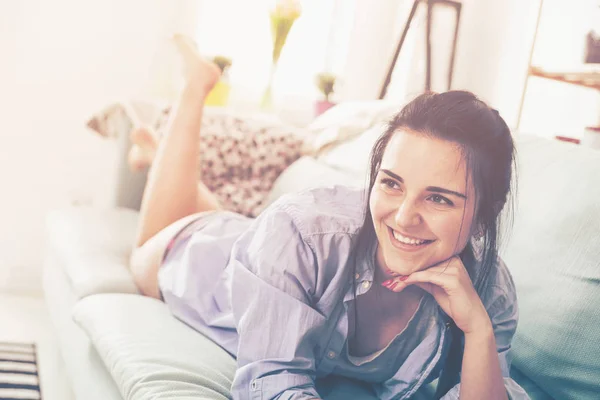 Молодая расслабленная женщина улыбается, лежа на удобном диване — стоковое фото