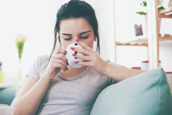 Молодая расслабленная женщина пьет кофе, сидя на удобном диване — стоковое фото