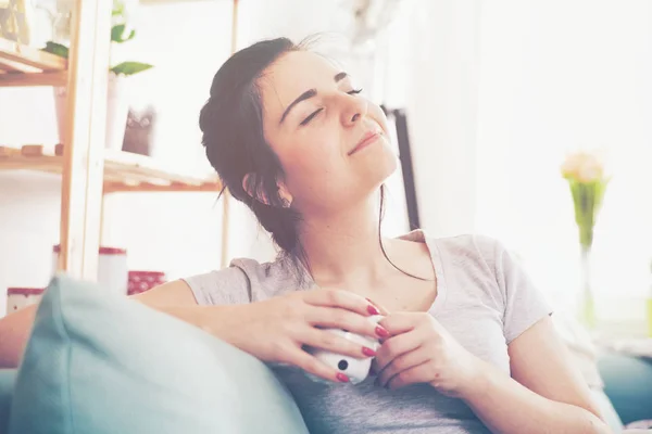 Ung avslappnad kvinna dricker kaffe medan du sitter på bekväm soffa — Stockfoto