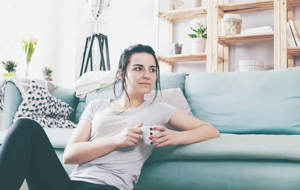 Молодая расслабленная женщина пьет кофе, сидя рядом с удобным диваном — стоковое фото