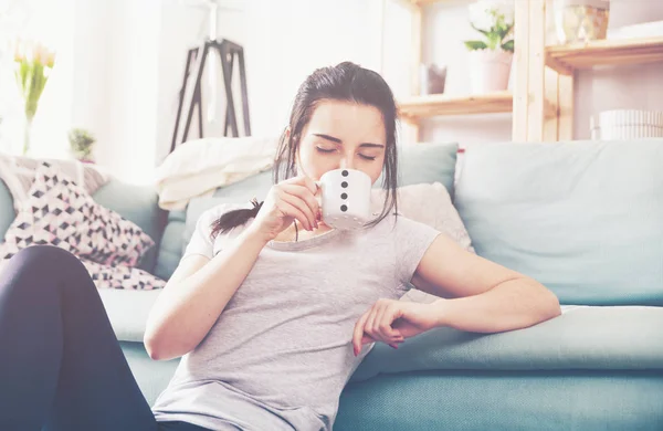 Junge entspannte Frau trinkt Kaffee, während sie in der Nähe eines bequemen Sofas sitzt — Stockfoto