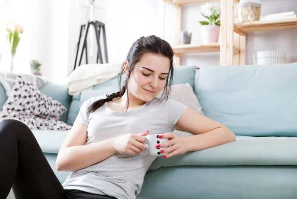 Jovem mulher relaxada bebendo café enquanto sentado perto de sofá confortável — Fotografia de Stock