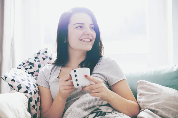 Junge entspannte, glückliche Frau trinkt Kaffee, während sie auf dem Sofa sitzt — Stockfoto