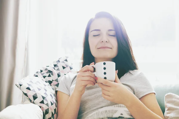 Ung avslappnat lycklig kvinna dricker kaffe medan du sitter på soffan — Stockfoto