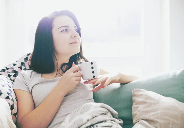 Junge entspannte, glückliche Frau trinkt Kaffee, während sie auf dem Sofa sitzt — Stockfoto