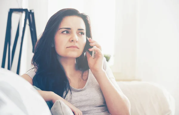 Unhappy worried woman talking on phone while sitting on sofa — Stock Photo, Image