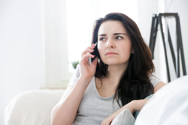 Несчастная обеспокоенная женщина разговаривает по телефону, сидя на диване — стоковое фото