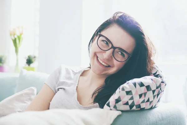 Relaxed young woman smiling while sitting on comfortable sofa — Stock Photo, Image