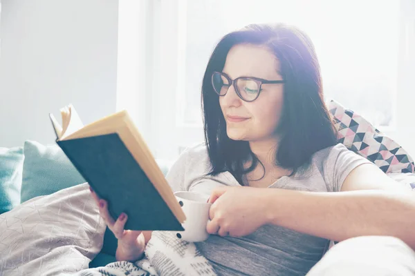 Entspannte Frau trinkt Kaffee und liest Buch zu Hause — Stockfoto