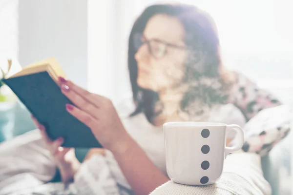 Entspannte Frau trinkt Kaffee und liest Buch zu Hause — Stockfoto