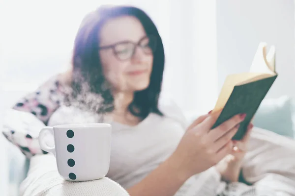 Mulher relaxada bebendo café e lendo livro em casa — Fotografia de Stock