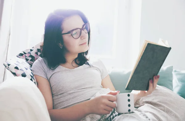 Nyugodt nő kávéfogyasztás és olvasás könyv otthon — Stock Fotó