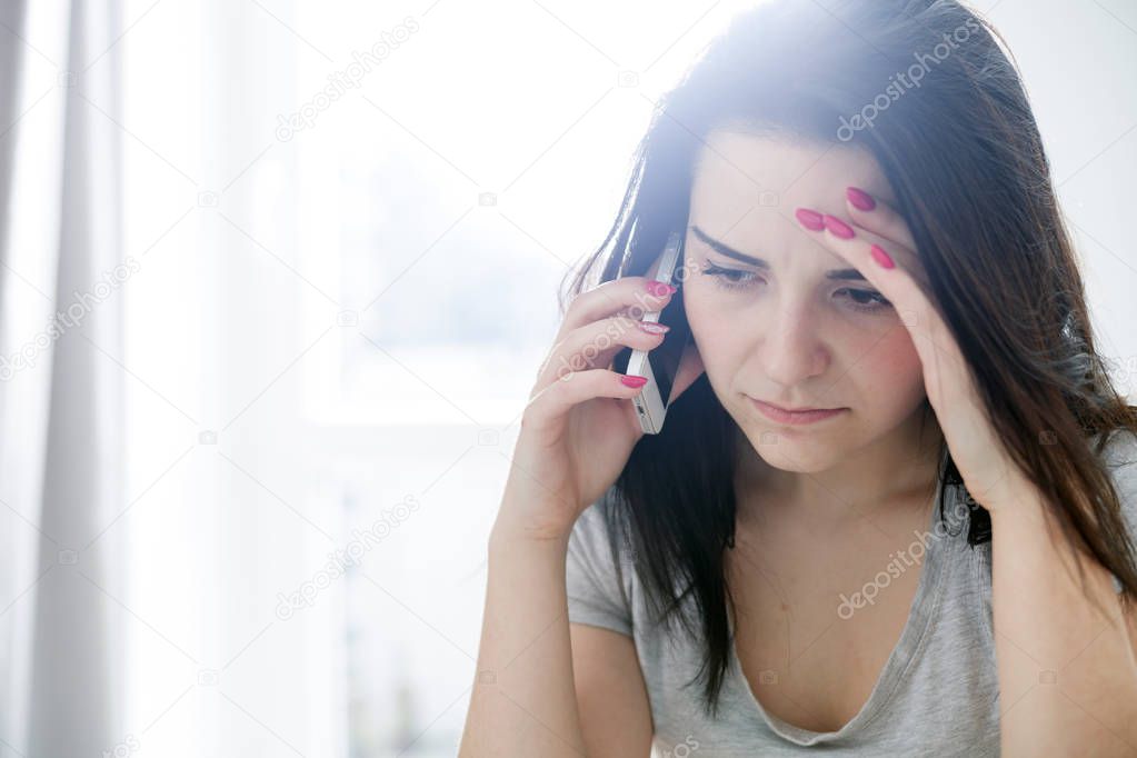 Unhappy worried woman talking on phone at home