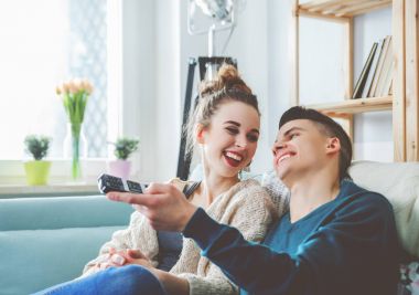 Sevgi dolu çift evde kanepe üzerinde tv izliyor ve gülüyor