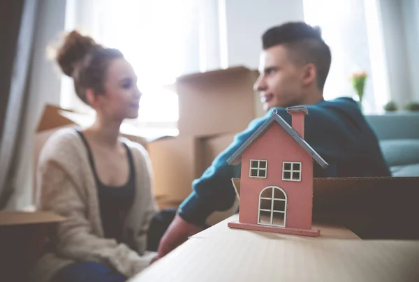 Coppia con casetta in legno nella loro nuova casa tra scatole di cartone — Foto Stock