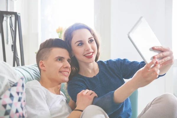 Pár kanapé otthon segítségével digitális tabletta, és így selfie — Stock Fotó