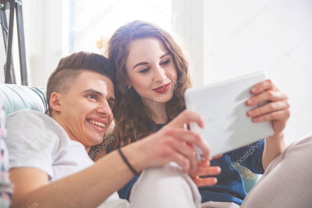 Couple on sofa at home using digital tablet and smiling