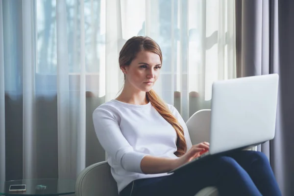 Hübsche Frau in modernem Hotelzimmer sitzt auf Sessel und benutzt Laptop — Stockfoto